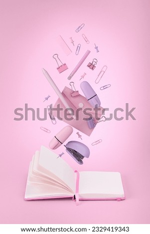 Pink and lilac stationery flying in  air against notebook. Pink background.