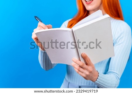 Red-haired woman in notebook studio photography writing on a blue background