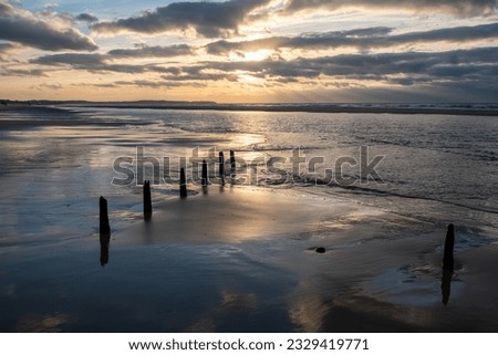 A compelling image showcasing a row of poles on the beach leading into the distance and the waves of the sea. The scene is heightened by a dramatic and colorful sunset sky, painting a striking picture