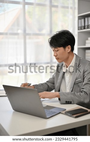A professional and focused Asian businessman in a formal business suit reading business reports and working on his business work at his desk in his private office.