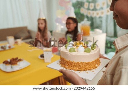 Cropped image of smiling birthday boy bringing cake with candle to table