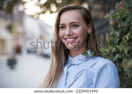 Close up portrait of a beautiful blonde woman outdoors on the street, leaning close to a barrier with ivy around it.