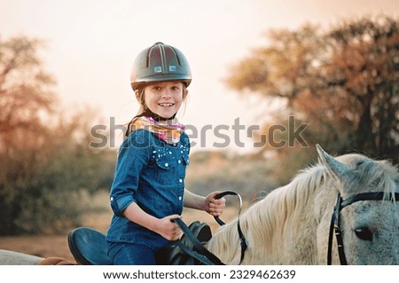 Young girl enjoying a horse back ride in the golden afternoon light. Riding on a white horse dressed in a denim shirt. Royalty-Free Stock Photo #2329462639