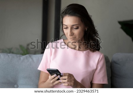 Close up Arabian woman using smartphone, sitting on couch, attractive young female holding phone, looking at screen, typing writing message, scrolling, chatting in social networks, shopping online