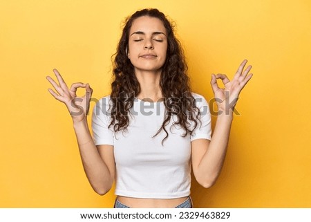Young Caucasian woman, yellow studio background, relaxes after hard working day, she is performing yoga.