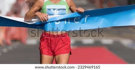 Woman running towards the finish line, female runner win the race outdoor in the city. Passes finish line as a winner Royalty-Free Stock Photo #2329469165