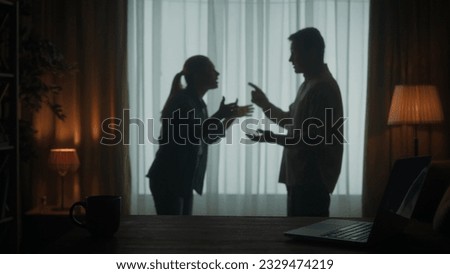 A man and a woman are arguing in the living room near the window. A silhouette of a couple arguing over the fact that the man spends too much time on the laptop. Royalty-Free Stock Photo #2329474219