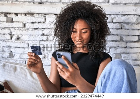 Relaxed afro-haired woman effortlessly shops online with credit card and phone at home. Royalty-Free Stock Photo #2329474449
