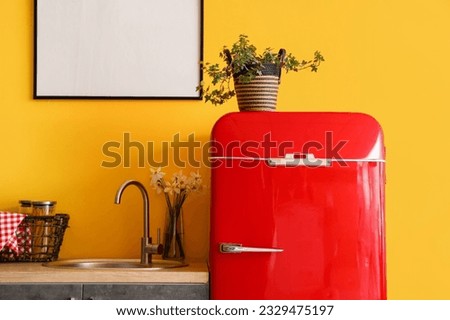 Interior of stylish kitchen with red fridge, blank picture and houseplant
