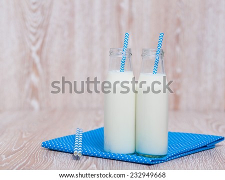 Two traditional glass bottles of milk with blue straws for drinking, standing on a blue napkin
