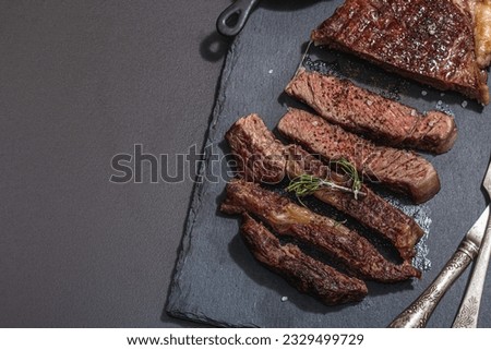 Well done roasting Ribeye steak with caramelized garlic and vintage cutlery. Trendy hard light, dark shadow, black stone concrete background, top view Royalty-Free Stock Photo #2329499729