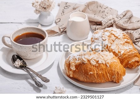 Good morning concept. Breakfast with cup of coffee and fresh croissant. Sweet creamy sauce, hard light, dark shadow. White wooden background, close up