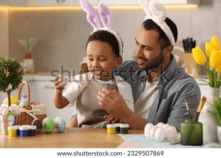 Happy African American father and his cute son painting Easter eggs at table in kitchen
