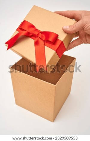 Male hand opening a brown present box with a red ribbon on a white background