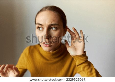 Portrait of anxious scared female stepping carefully eavesdropping with anxious facial expression, listening to strange scary sounds attentively, holding hand around ear isolated on gray background Royalty-Free Stock Photo #2329525069