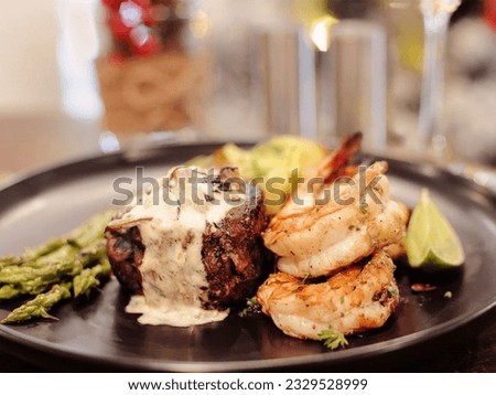 Grilled Tiger shrimps, beef tenderloin topped creamy Mushroom Sauce, mashed potatoes, asparagus. Isolated on a black background. Close-up. Macro. Selective focus. American cuisine. Royalty-Free Stock Photo #2329528999