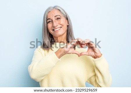 middle age gray hair woman smiling and feeling happy, cute, romantic and in love, making heart shape with both hands Royalty-Free Stock Photo #2329529659