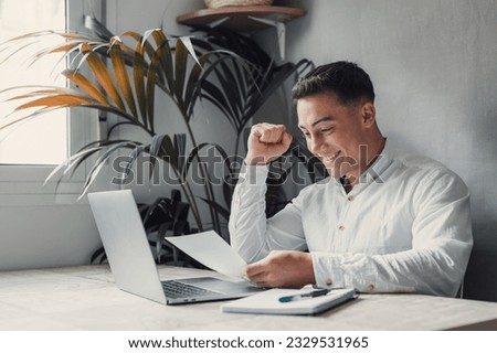 Excited business man student reading postal mail letter overjoyed by great news, happy male winner holding paper bill with loan approval celebrate taxes refund receive salary rise payment sit at desk Royalty-Free Stock Photo #2329531965