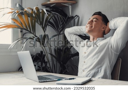 Calm millennial man in glasses sit relax at home office workplace take nap or daydream. Happy relaxed Caucasian young male rest in chair distracted from computer work, relieve negative emotions. Royalty-Free Stock Photo #2329532035