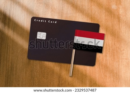 The Flag of Yemen and Black Credit Card on Wooden Background.