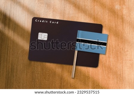 The Flag of Botswana and Black Credit Card on Wooden Background.
