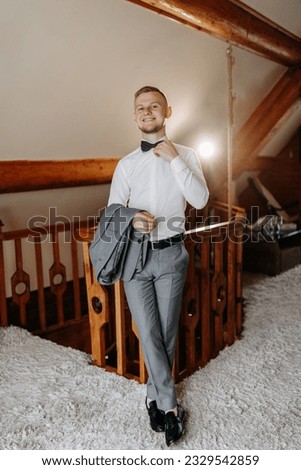 A young businessman in a hotel room is dressed in a classic gray suit, a white shirt and a bow tie. Rest in wonderful apartments. Groom's morning at the hotel. Male hands close up