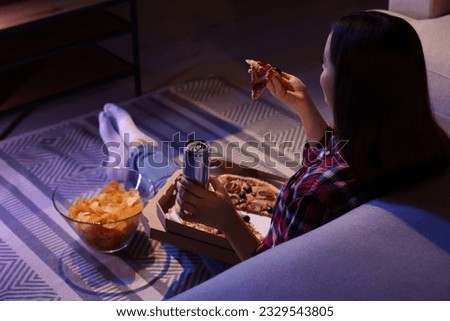 Young woman eating pizza while watching TV in room at night. Bad habit Royalty-Free Stock Photo #2329543805