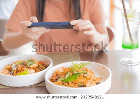 A woman eat  lunch with feeling happy and enjoy to eat shrimp spaghetti stir fry in the restaurant with taking photo by mobile phone, Enjoy eating concept. Take a photos.