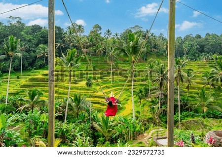 Young female tourist in red dress enjoying the Bali swing at tegalalang rice terrace in Bali, Indonesia Royalty-Free Stock Photo #2329572735