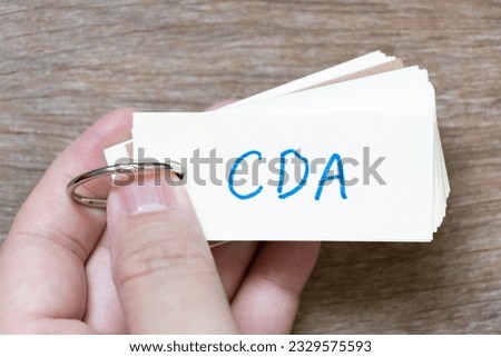Hand hold flash card with handwriting in word CDA (Abbreviation of Confidential disclosure agreement) on wood background