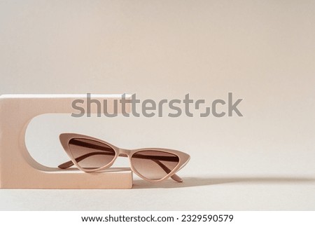 Glamour cat eye frame sunglasses on a podium on beige background. Women's Trendy sunglasses still life in minimal stile. Fashionable eyewear accessories. Optic store discount, sale, offer. Copy space Royalty-Free Stock Photo #2329590579