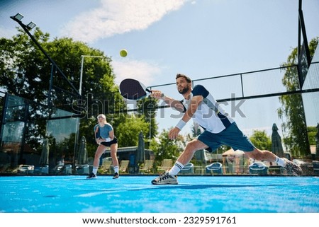 Young athlete playing padel in mixed doubles on outdoor court. Copy space. Royalty-Free Stock Photo #2329591761