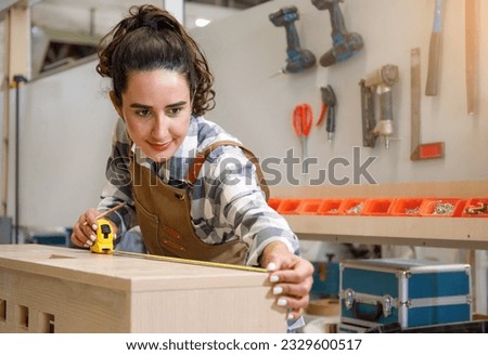Young Latin female carpenter using a tape measure to measure dimensions to cut wood. to make furniture in the carpentry workshop Concept of young people start up and SME small business concept Royalty-Free Stock Photo #2329600517