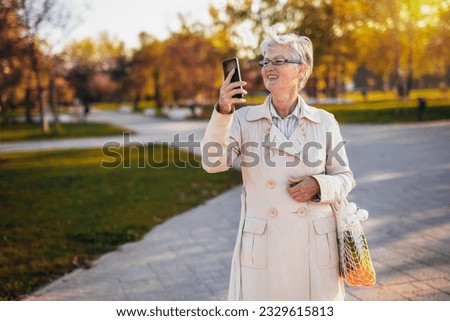 An older woman walking in the park and taking pictures of it with her groceries in the autumn
