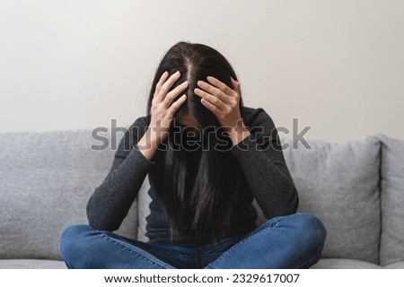 Unhappy anxiety young Asian woman covering her face with pillow on the cough in the living room at home. Royalty-Free Stock Photo #2329617007