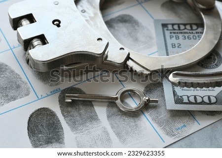 Handcuffs laying on fingerprint card with money - concept for arrest bail money  Royalty-Free Stock Photo #2329623355