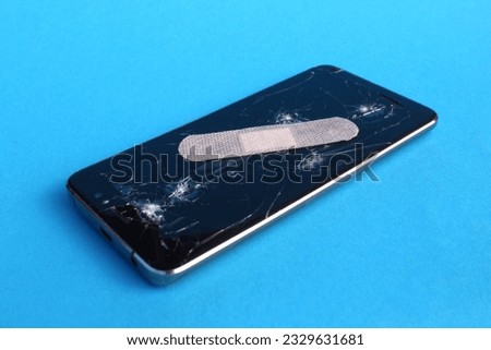 On a blue background lies a broken phone sealed with adhesive tape.