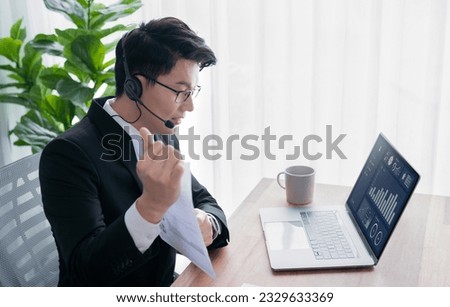 Confident asian telesales businessman work in modern office wearing headphone, presenting BI dashboard analysis to clients and customers in online meeting. Success modern telesales business . Jubilant Royalty-Free Stock Photo #2329633369