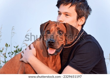 Portrait of young man hugging his lovely Rhodesian ridgeback dog. Royalty-Free Stock Photo #2329651197