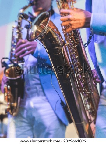 Concert view of saxophonist in a blue and white suit, a saxophone sax player with vocalist and musical band during jazz orchestra show performing music on stage in the scene lights Royalty-Free Stock Photo #2329661099