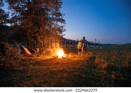 Two tourists rest in nature in the evening by the fire