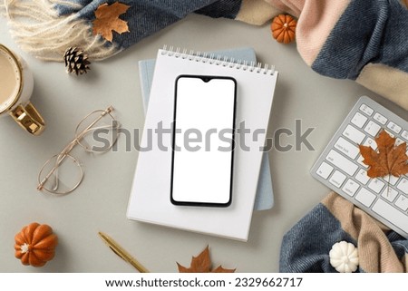 Experience coziness of freelance work in autumn with this top view picture featuring phone on notepad, gilded pen and glasses, keyboard and autumnal decor on grey isolated background with copyspace