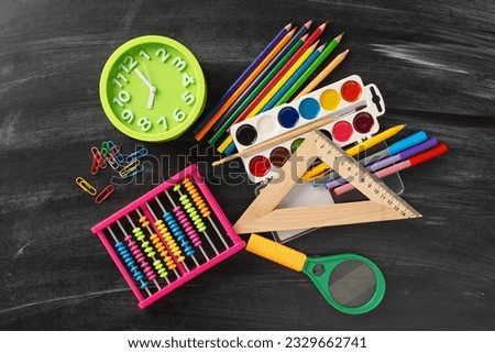 Explore the magic of early childhood education with this creative top-down perspective: a captivating selection of child school supplies such as abacus, paints, clock on blackboard isolated background