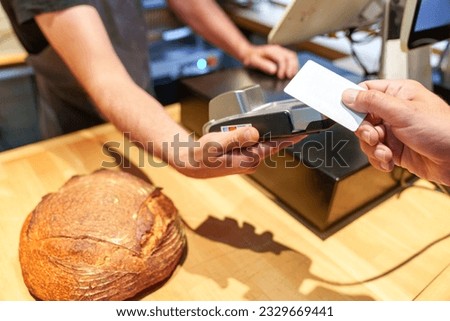 An anonymous bakery worker's hands use a card reader to accept payment from a customer for a loaf of bread.