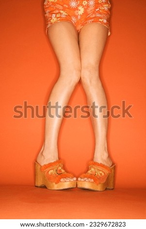 Legs and feet of Caucasian mid-adult woman standing pigeon-toed in chunky shoes on orange background.