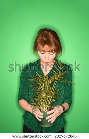 Caucasian mid-adult woman on green background looking at plant.