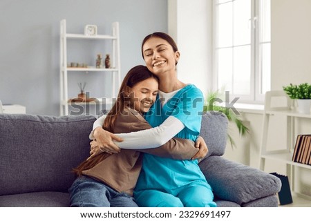 Happy child hugs doctor. Happy, smiling woman pediatrician in uniform and little girl patient sitting on couch at home and hugging. Healthcare, home visit, love, care, help, support, gratitude concept