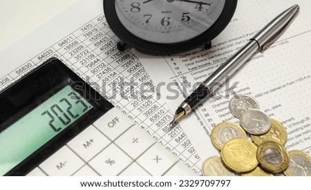 Word 2023 on calculator display with alarm clock, coins and pen
