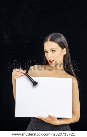 makeup artist holds an empty billboard in his hands on a dark background and points to it with a brush
