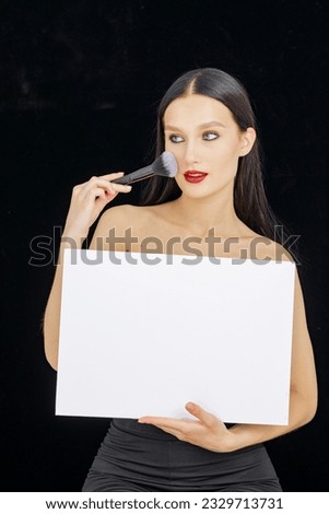 makeup artist holds an empty billboard in his hands on a dark background and points to it with a brush